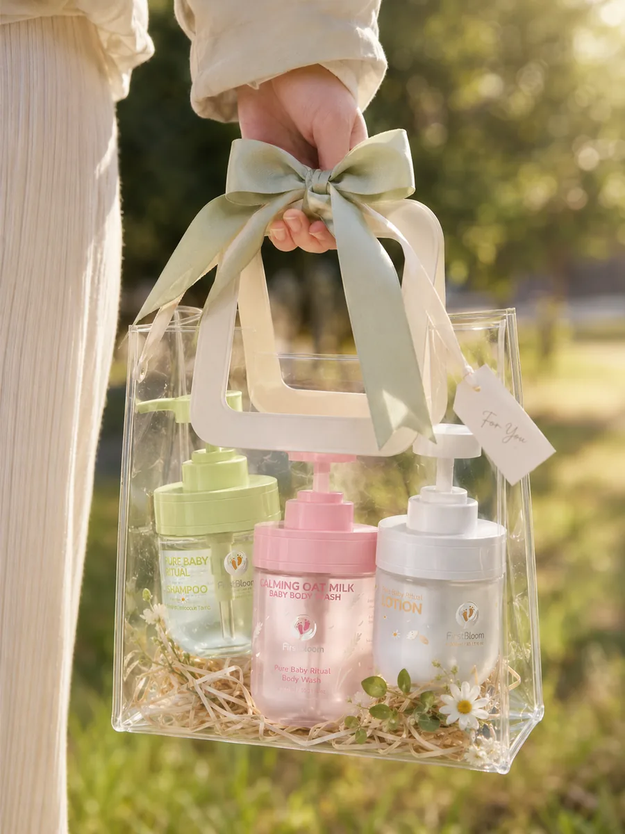 FirstBloom baby shampoo, body wash and lotion pump bottles carried in a clear gift bag with a sage ribbon.