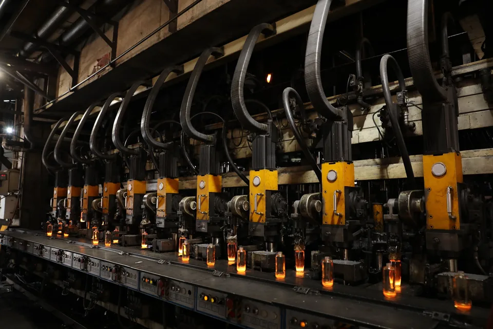 Glass bottle forming line in production, with glowing hot bottles leaving the molds.