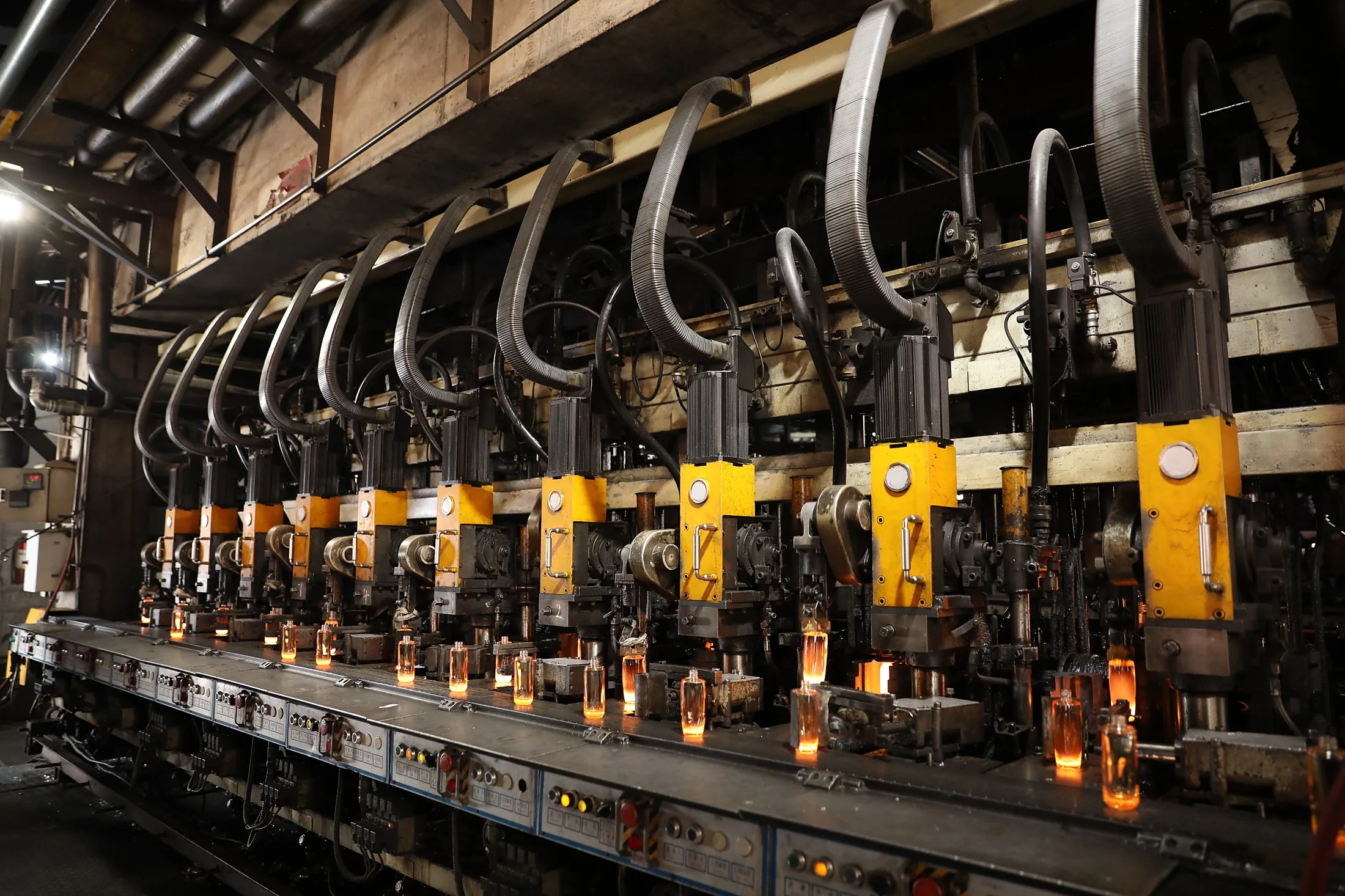 Row of glass forming machines with glowing bottles leaving the molds