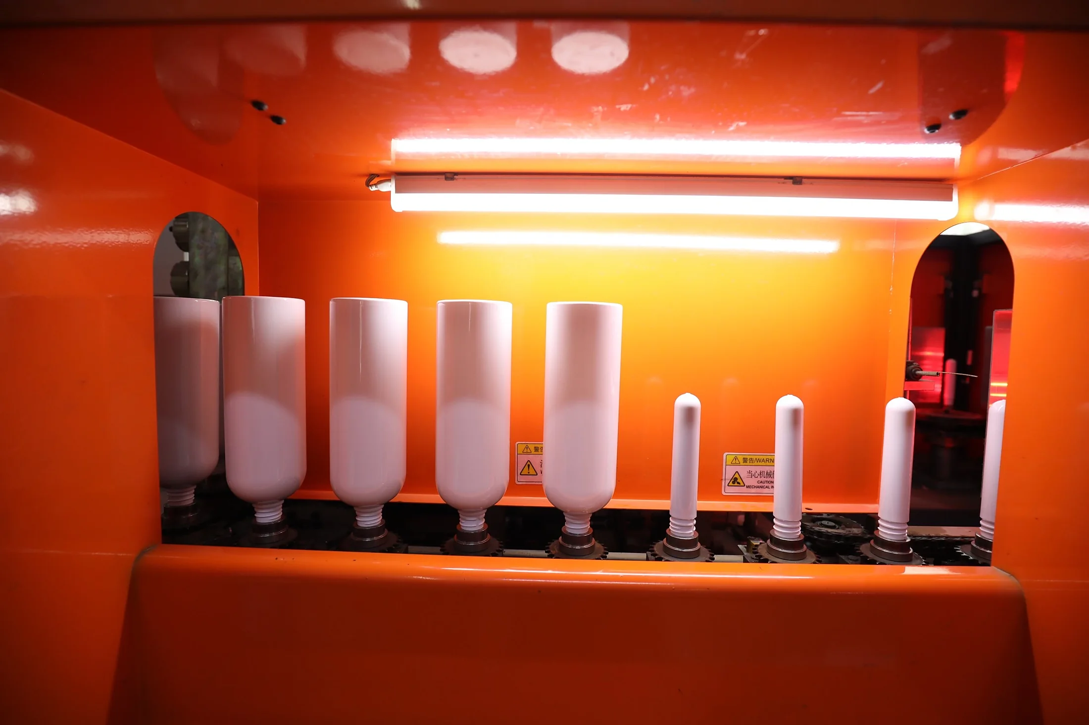 White PET preforms and blown bottles inside a stretch blow molding machine